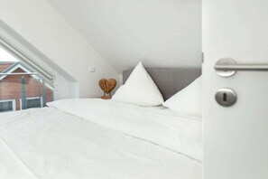 A bedroom with a bed, pillows, a bedside table, and a view of a building outside. - Apartment in Juist with Wi-Fi and water park (Juist)