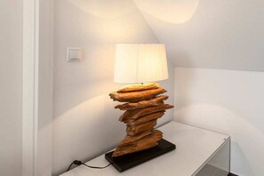 Une lampe moderne dotée d’un pied en bois original et d’un abat-jour blanc, posée sur une table blanche.