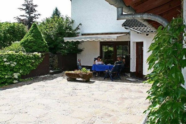 A courtyard with a stone floor, a table with chairs, and a person seated. - Holiday apartment with 1 bedroom (Walsdorf-Zilsdorf)