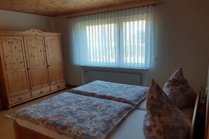 A room with two beds, a wooden wardrobe, and a window with sheer curtains. - Holiday apartment with 1 bedroom (Walsdorf-Zilsdorf)