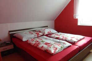 Un llit individual amb matalàs vermell i roba de llit floral en una habitació amb parets vermelles i un sostre inclinat.
