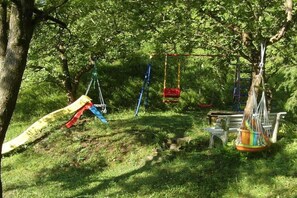 Ein Spielplatz mit Schaukeln und einer Rutsche, umgeben von Bäumen und Gras.