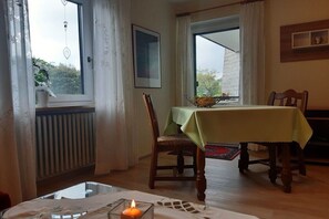 Uma área de refeições com mesa posta para dois, uma cadeira, janela com cortinas e radiador.