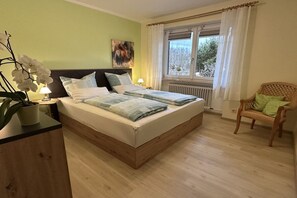A bedroom with a bed, a chair, a window with curtains, and a radiator. - Holiday apartment with 1 bedroom (Fichtelberg)