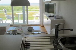 A kitchen with a view of the sea, a dining area with chairs and a table, and a television. - Holiday apartment with 1 bedroom (Cuxhaven)