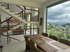Un intérieur moderne avec un escalier, un coin repas et une grande fenêtre donnant sur la ville.