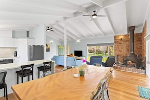 A modern kitchen with white cabinetry, a dining area with a wooden table and chairs, a living room with a blue sofa, and a fireplace. - Isle Grove - Close to Cowes Beach (Cowes)