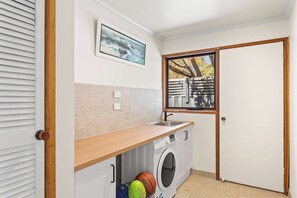 A compact laundry room with a washing machine, a sink, and a window with a view of trees. - Isle Grove - Close to Cowes Beach (Cowes)
