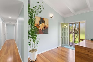 Corredor com piso de madeira, planta em vaso, pintura e porta que dá para área externa.