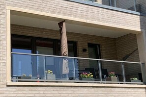 Ein Balkon mit Glasgeländer, Topfpflanzen und einem braunen Sonnenschirm.