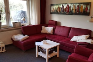 Un canapé rouge, une table d’appoint blanche et un tableau représentant des voiliers accroché au mur.