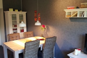 A dining area with a table, chairs, a cabinet, and wall-mounted shelves. - Holiday apartment with 1 bedroom (Borkum)
