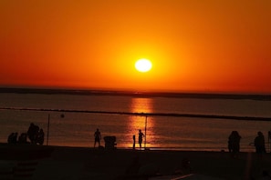 Ein Sonnenuntergang über dem Wasser, mit Silhouetten von Personen und Booten.
