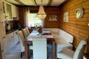 Ein Interieur einer Holzhütte mit einem Esstisch, Stühlen, einer Kandelaber und einer Uhr an der Wand.