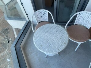 Ein Balkon mit Glastür, zwei weißen Korbstühlen und einem runden Tisch mit Sitzkissen.