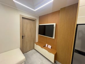 Een moderne badkamer met een houten wastafelmeubel, een wandgemonteerde televisie en een deur.