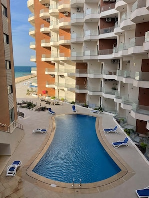 Un edifici d'apartaments modern amb piscina, balcons i vistes a la platja.