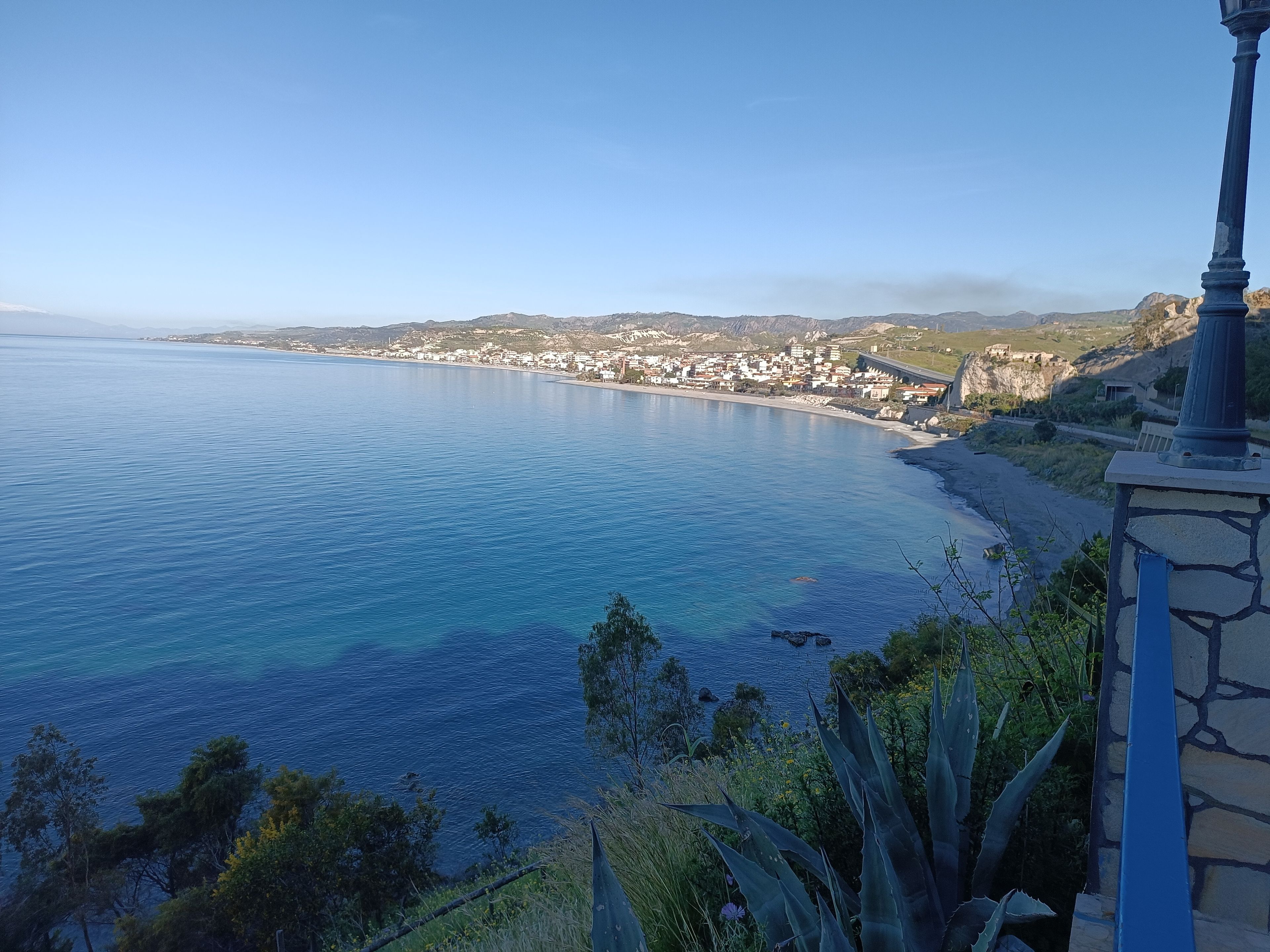 A coastal town with a clear view of the sea, a stone structure, and surrounding vegetation.