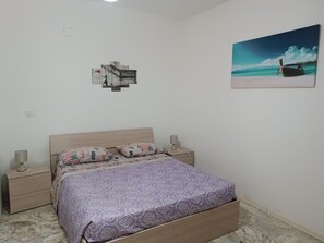 A bedroom with a bed, two bedside tables, a nightstand, a wall-mounted picture, and a marble floor. - Blue Vacation Home (Bova Marina)