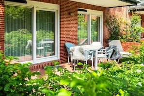 A patio with a table and chairs, a brick wall, and a sliding glass door. - Holiday apartment in Juist with swimming pool (Juist)