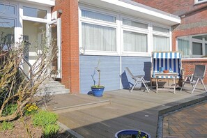 A residential garage with a blue door, a potted plant, and outdoor seating with a striped awning. - Holiday apartment with 1 bedroom (Norderney)
