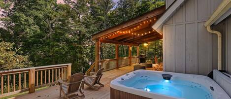 A wooden deck with a hot tub, outdoor furniture, and a covered area with string lights.