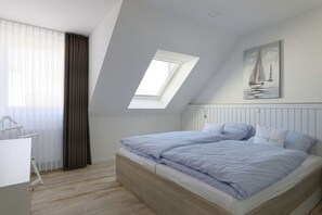 Een slaapkamer met een schuine kap, dakraam, een bed met bijpassende kussens en een schilderij van een zeilboot aan de muur.