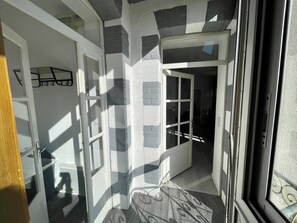 Una habitación con una puerta que da a un interior oscuro, una ventana con vistas al exterior y una pared con un diseño texturizado.