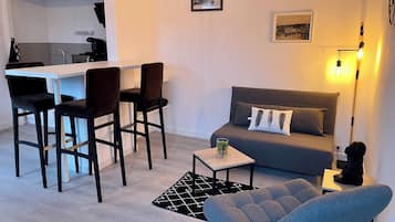Een knus woongedeelte met een kitchenette, een bank, een salontafel en een eethoek met stoelen.