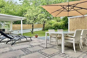 An outdoor patio area with a table and chairs, a sun lounger, and a large umbrella. - Apartment in Herrsching with swimming pool (Herrsching)