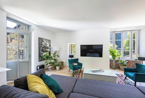 A modern living room with a grey sofa, teal armchairs, and a flat-screen TV mounted on the wall. - House on the Riverbank in Downtown with a Pool (Vitré)
