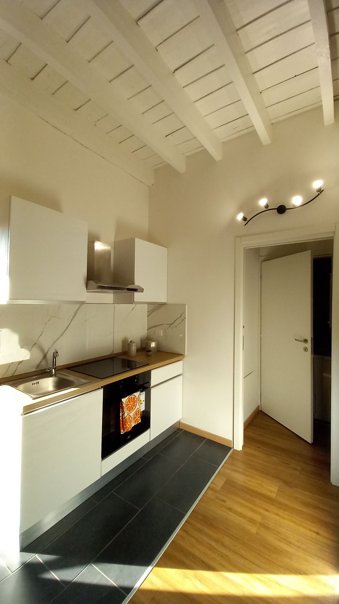 Een moderne keuken met witte kasten, een zwart aanrecht en een houten vloer.