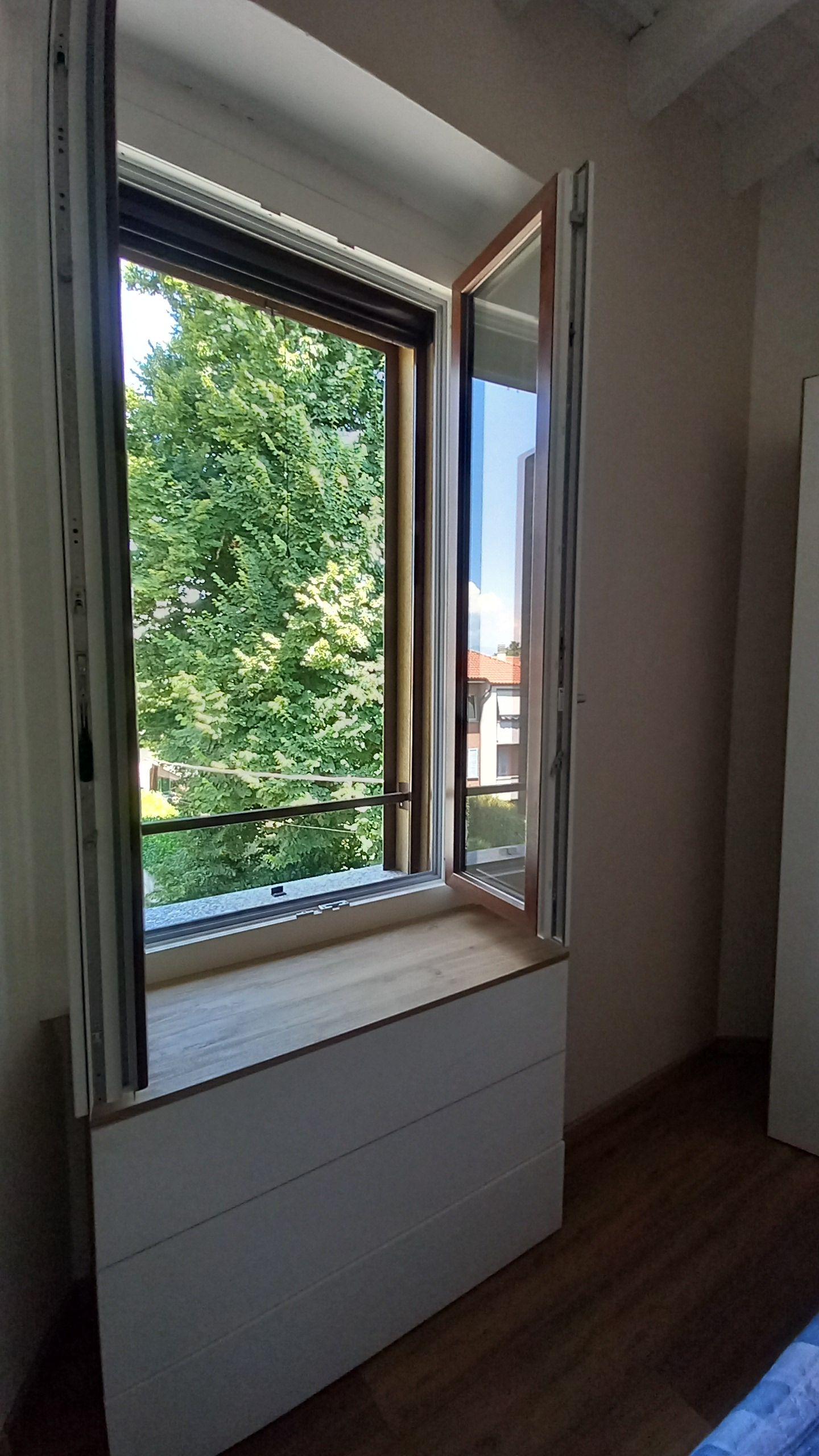 Huone, jossa on ikkuna, puulattia ja valkoinen seinä.