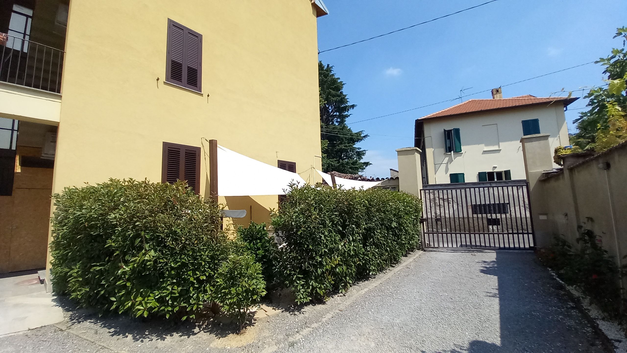 Una stretta via con un edificio giallo a sinistra e uno bianco a destra. Al centro, un cancello.