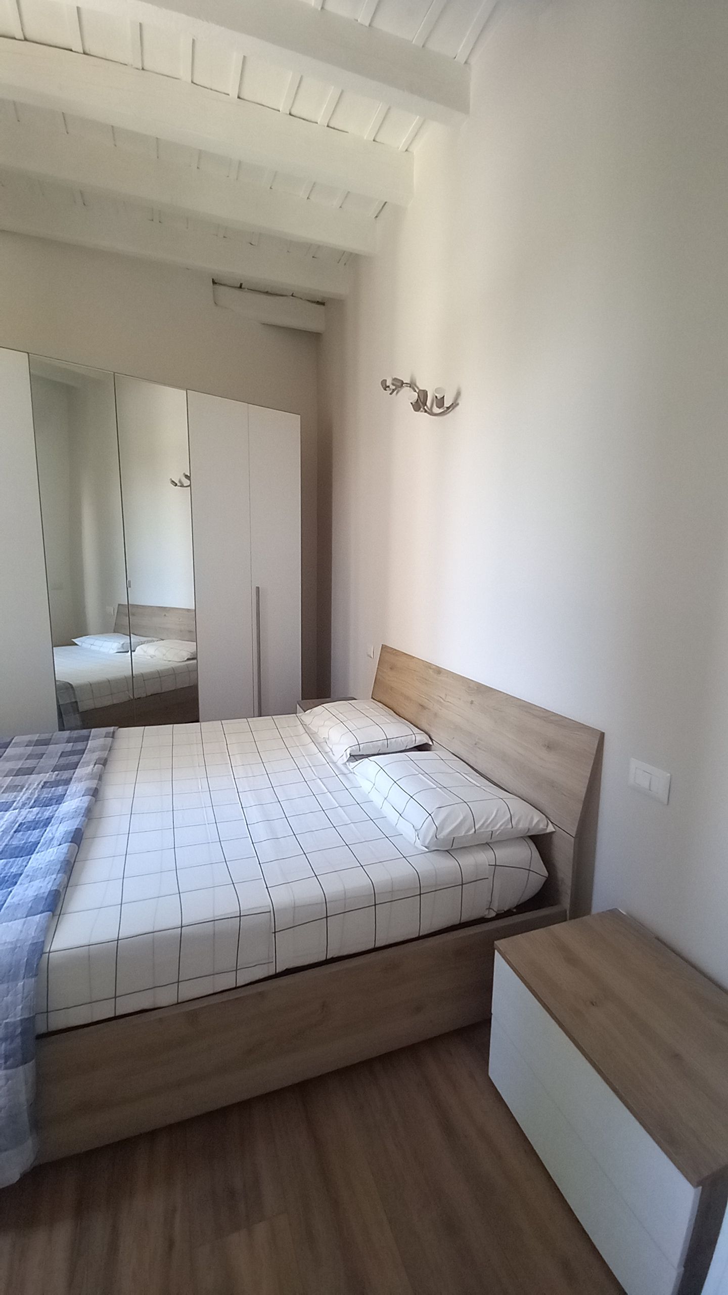 Een slaapkamer met een houten bed, een kledingkast en een spiegel.