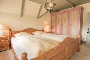 A bedroom with a wooden bed, two bedside tables with lamps, and a pink wardrobe with floral designs. - Friesenhaus Sara (S1) (Wenningstedt)