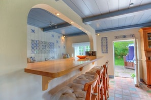 A kitchen with a long counter, bar stools, and a view to the outside. - Friesenhaus Sara (S1) (Wenningstedt)