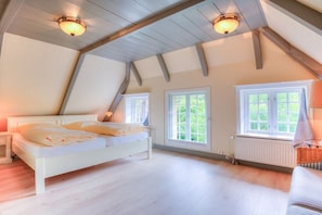 A bedroom with a sloped ceiling, a bed, two windows, and a radiator. - Friesenhaus Sara (S1) (Wenningstedt)