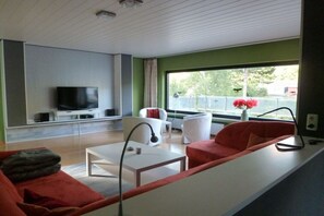 A modern living room with a flat-screen TV, white furniture, and a large window with a view of greenery. - Holiday home with 5 bedrooms (Schleiden-Gemünd)