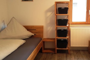 Ein Einzelbett mit Holz Kopfteil, ein kleiner Nachttisch aus Holz und eine integrierte Regaleinheit mit Aufbewahrungsboxen.