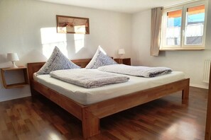 A double bed with a wooden frame, two bedside tables with lamps, a window with curtains, and a painting on the wall. - Holiday apartment with 2 bedrooms (Sonthofen)