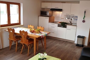 Ett kompakt kök med vita skåp, en mikrovågsugn och en matplats med ett bord för fyra personer.