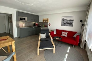 A compact living space with a kitchenette, a red sofa, a wooden dining table, and a grey rug. - Alpenflair holiday apartment 235 (Oberstdorf)