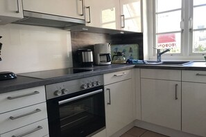 A kitchen with white cabinets, a black stove, and a coffee maker. - Holiday home in Norddorf with swimming pool (Norddorf)