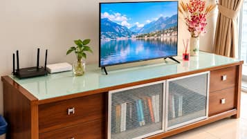 Un meuble TV en bois avec un plateau en verre, un téléviseur à écran plat et un vase rempli de fleurs.