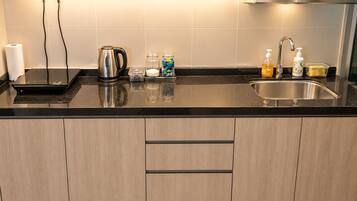 A modern kitchen with a black countertop, stainless steel kettle, and a sink with soap dispenser.