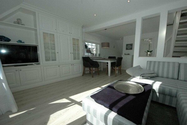 A modern living room with a television, a dining area with chairs, and a sofa with a decorative tray. - Risgap holiday apartment 11c/5 (Wenningstedt)