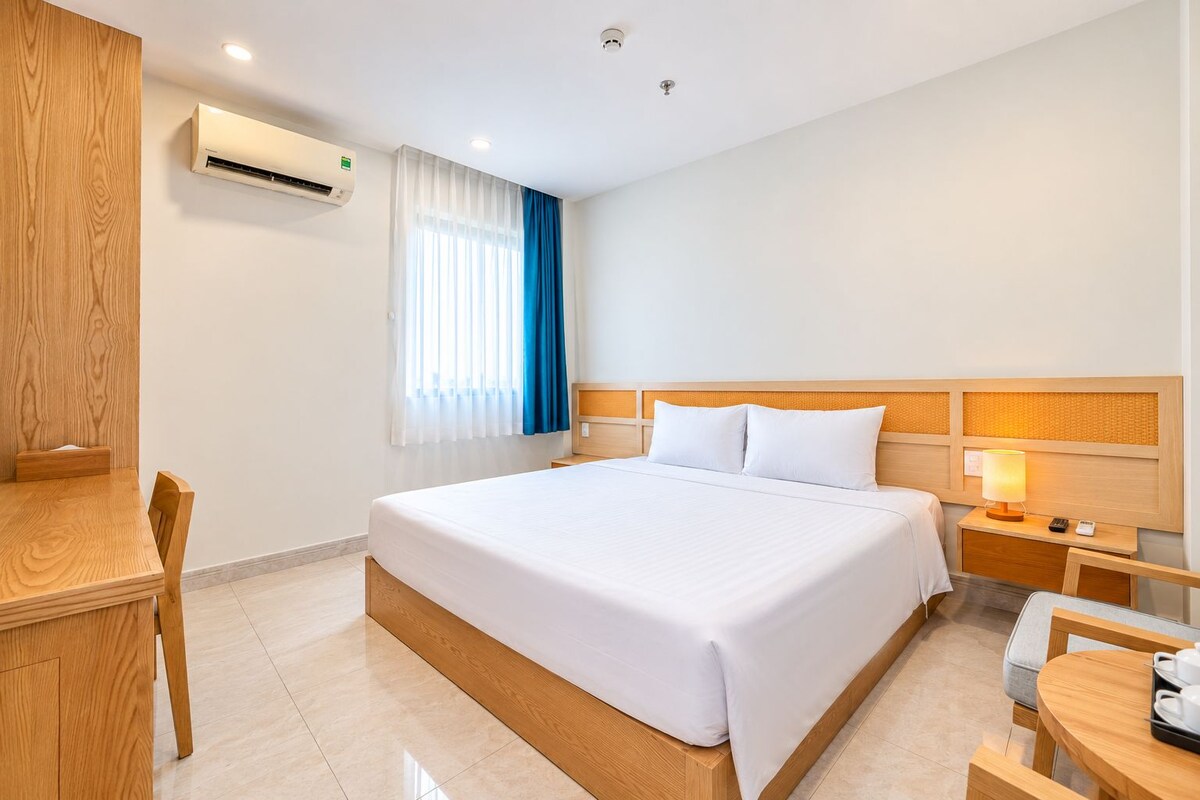 Ein Hotelzimmer mit einem großen Bett, einem Schreibtisch, einem Stuhl, einem Nachttisch mit Lampe und einer Klimaanlage.