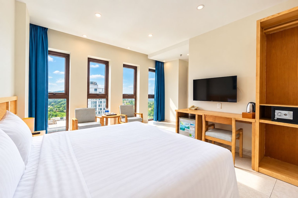 A hotel room with a large bed, a desk with a television, and a view of the outdoors.