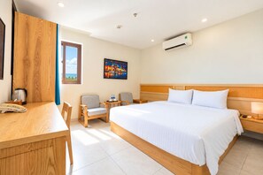 Ein Hotelzimmer mit Bett, Schreibtisch, zwei Stühlen, einem Nachttisch, einer Klimaanlage und einem Bild an der Wand.